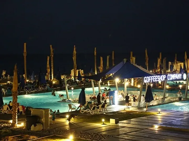 Pool lit at night beside a coffee shop and shaded seating